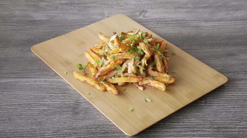 Masala fries on a wooden board, topped with herbs and sauce.